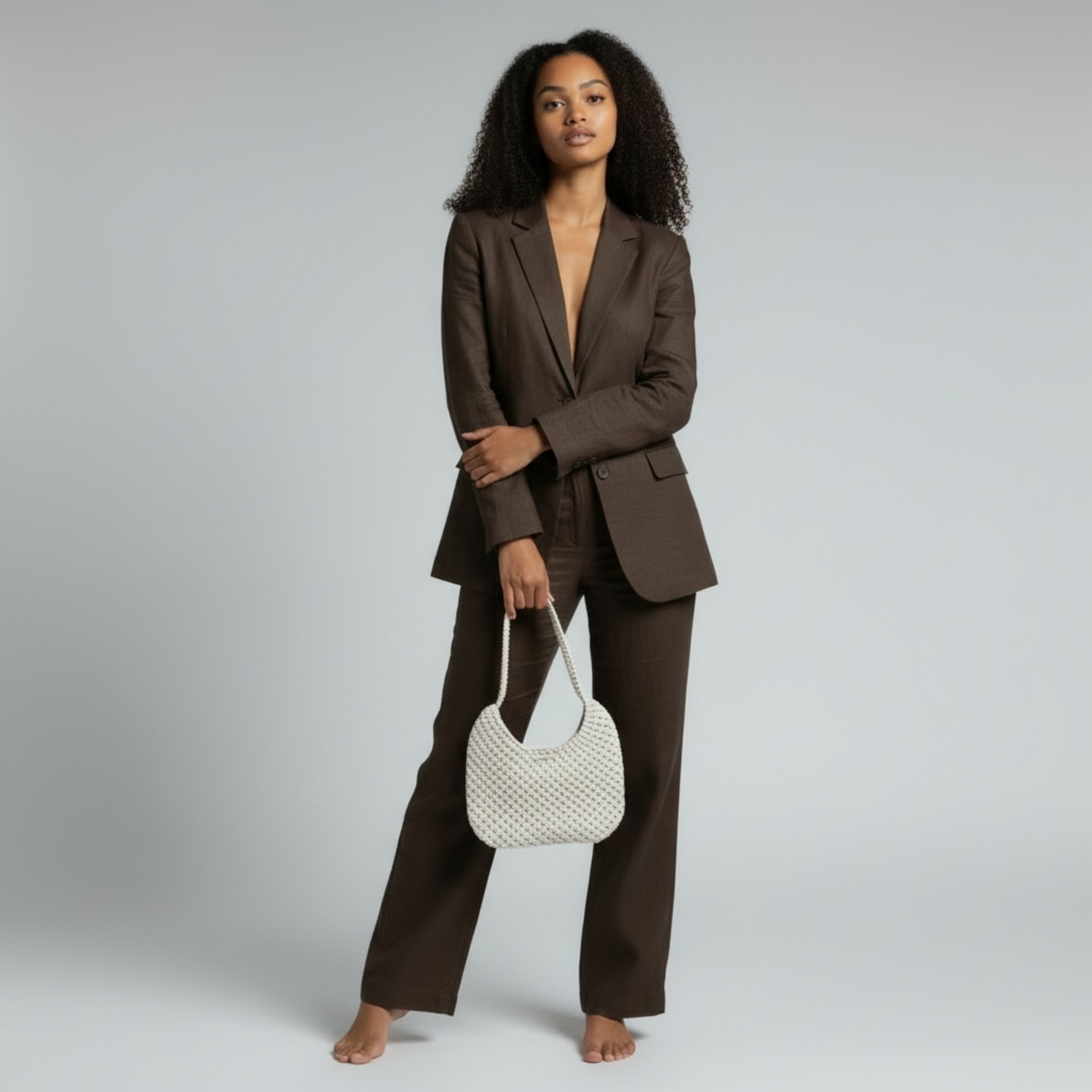Woman holding beige macrame shoulder bag with brown suit, minimalist luxury style