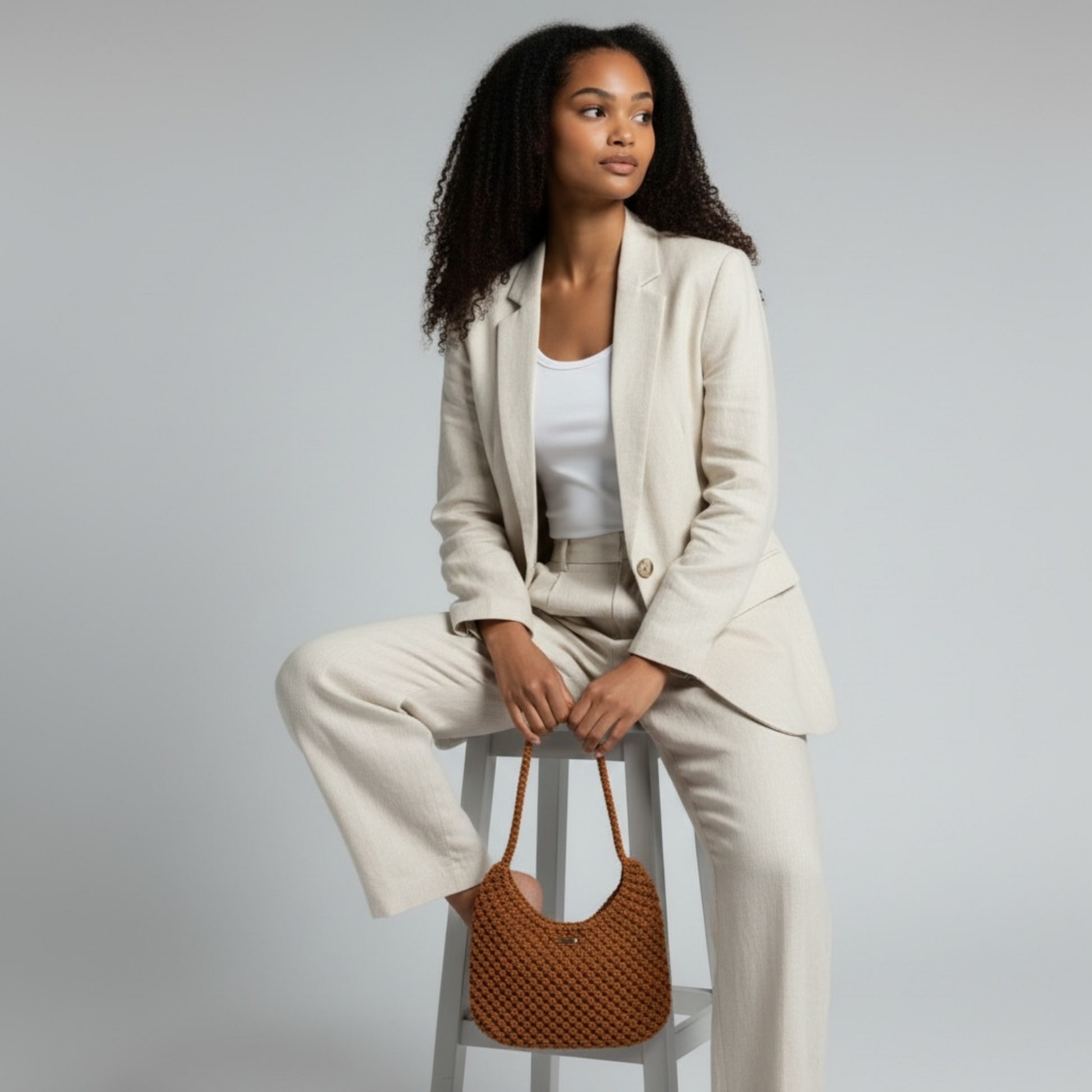 Burnt orange macrame half moon bag held by seated model, soft structured silhouette with artisan texture