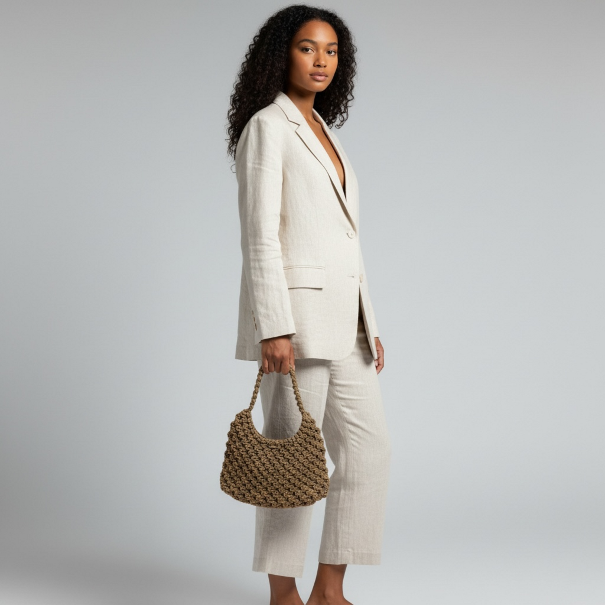 Model holding a caramel brown macrame half moon bag styled with neutral tailored outfit