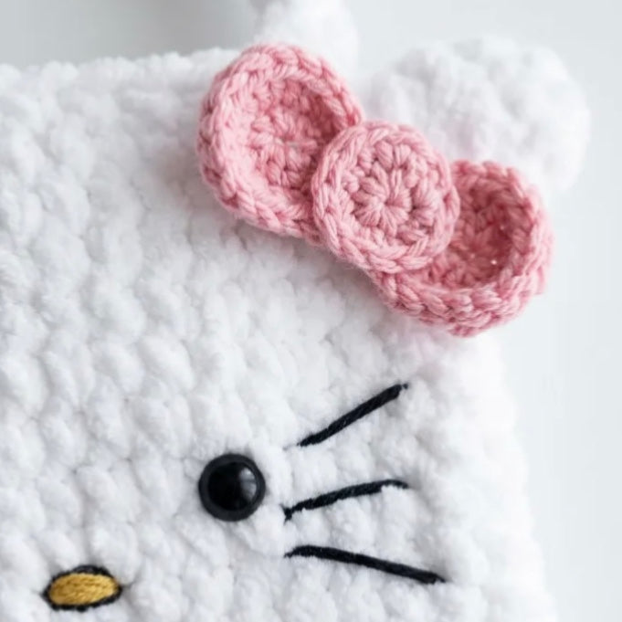 Close-up of the pink crochet bow, white stitches and embroidered face on a Hello Kitty bag.