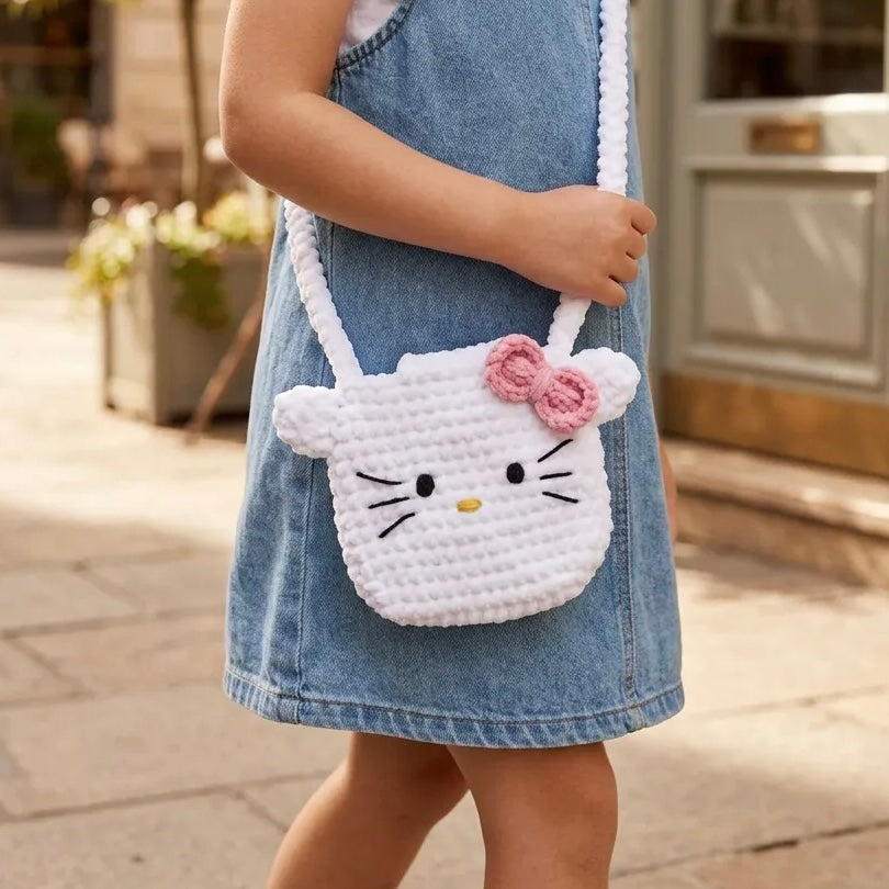 Child in a denim dress wearing a white Hello Kitty crochet bag with a pink bow and long white strap.