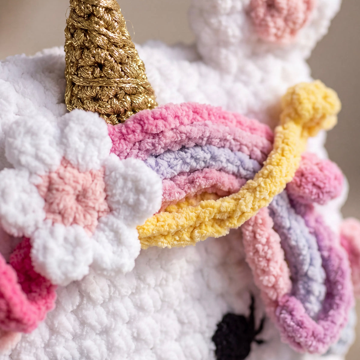 Close-up of a unicorn crochet bag showing the white yarn texture, gold horn, pink flower and pastel-colored mane.